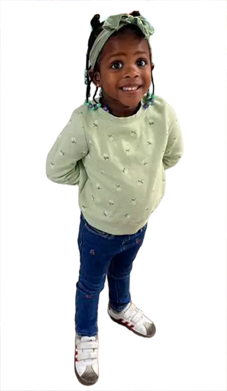 Full-body image of a smiling young Black girl wearing a light green floral shirt, blue jeans, and sneakers, with a green h...